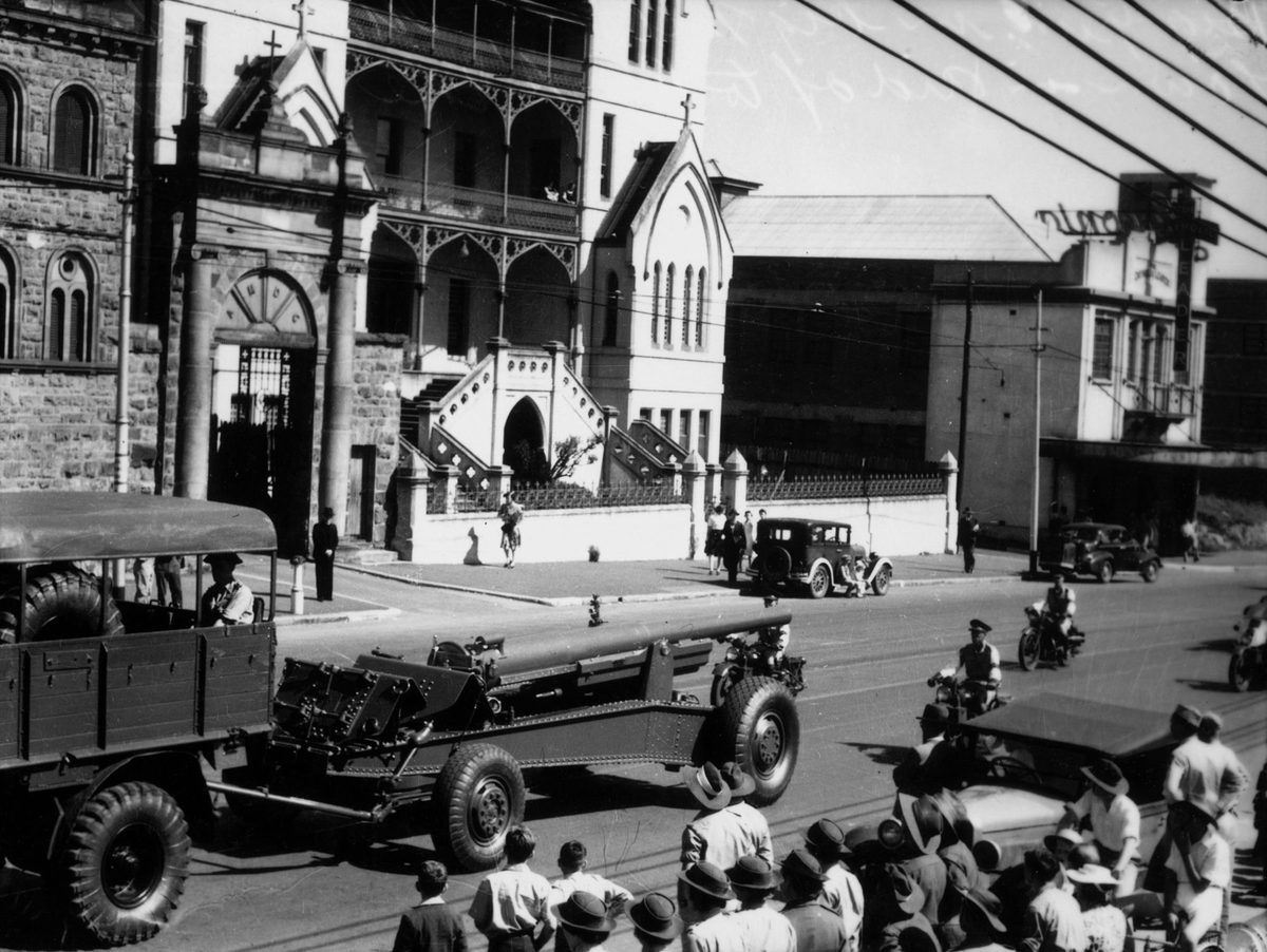 Gun carriage being towed along behind an Army truck in a street parade,Brisbane, July 1942