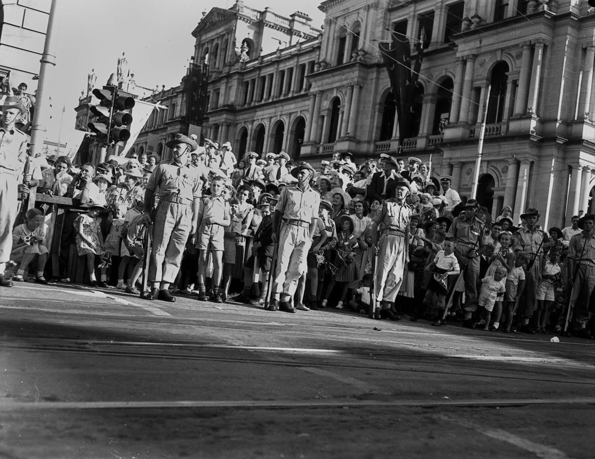 Small children peer out from between the soldiers while waiting for Queen Elizabeth II and Prince Philip to pass, March 1954