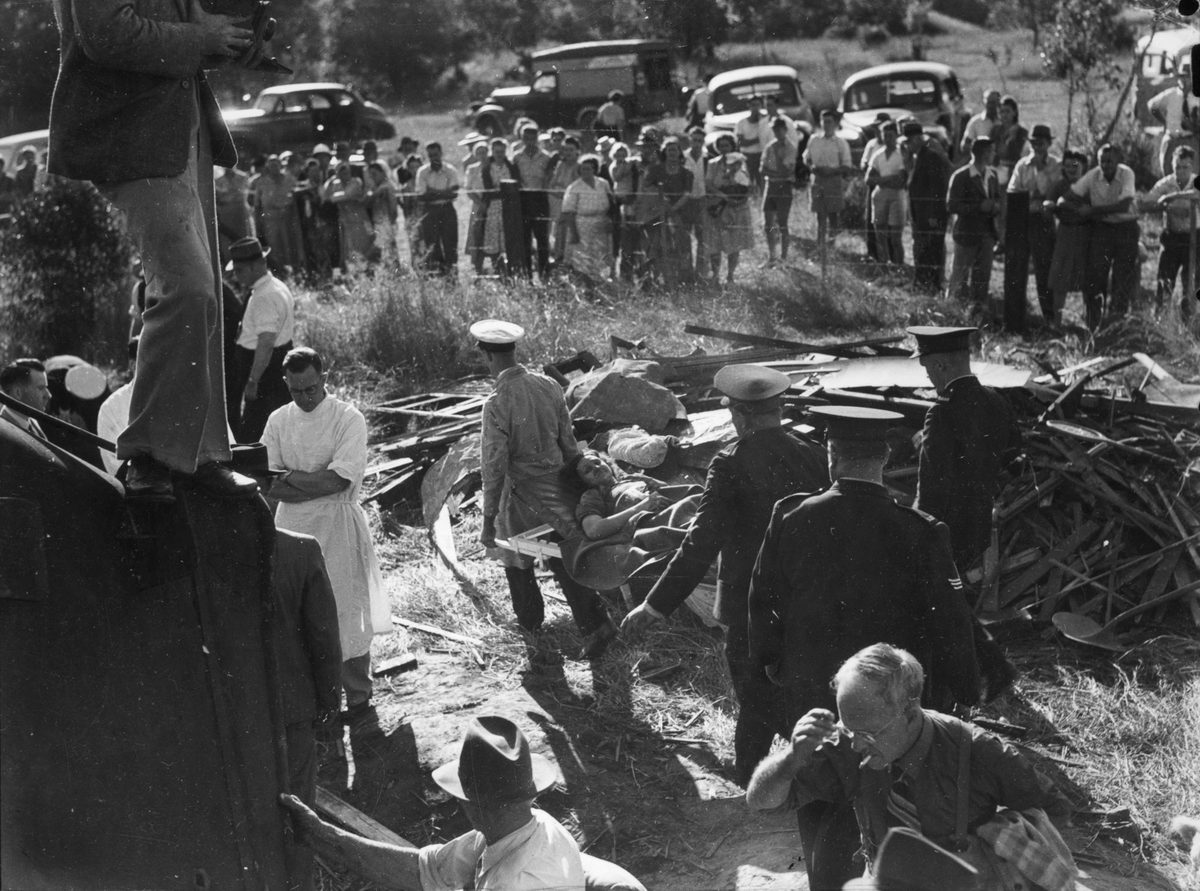 Female train accident survivor is carried away by rescue workers at Camp Mountain, 1947
