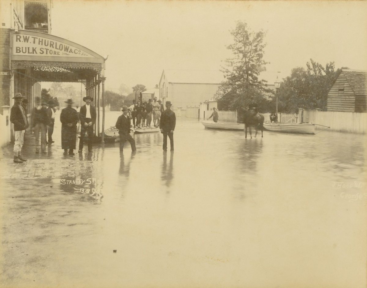 Gathering of men and boats in the flooded street outside Thurlow's bulk store, South Brisbane, 1890