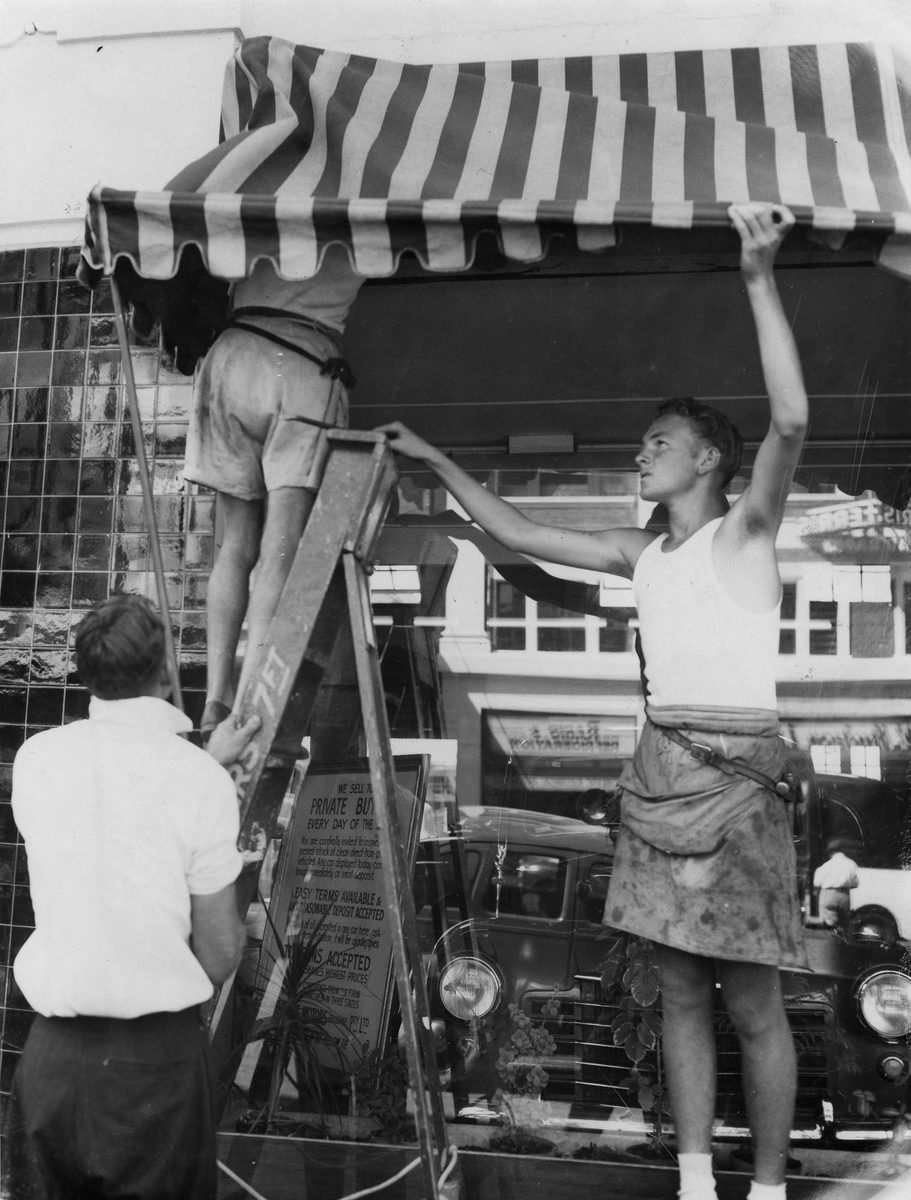 Council workmen pulling down a canvas awning infront of Christeys Motors, Adelaide Street, Brisbane, 1953