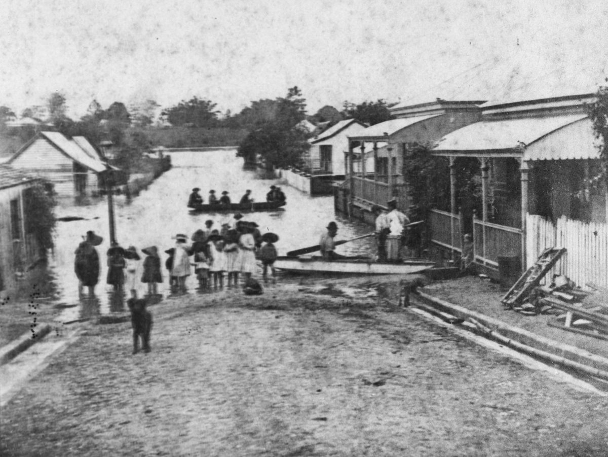 Onlookers watch as people are ferried across a flooded street in a dinghy during the 1890 floods at Kangaroo Point, Brisbane