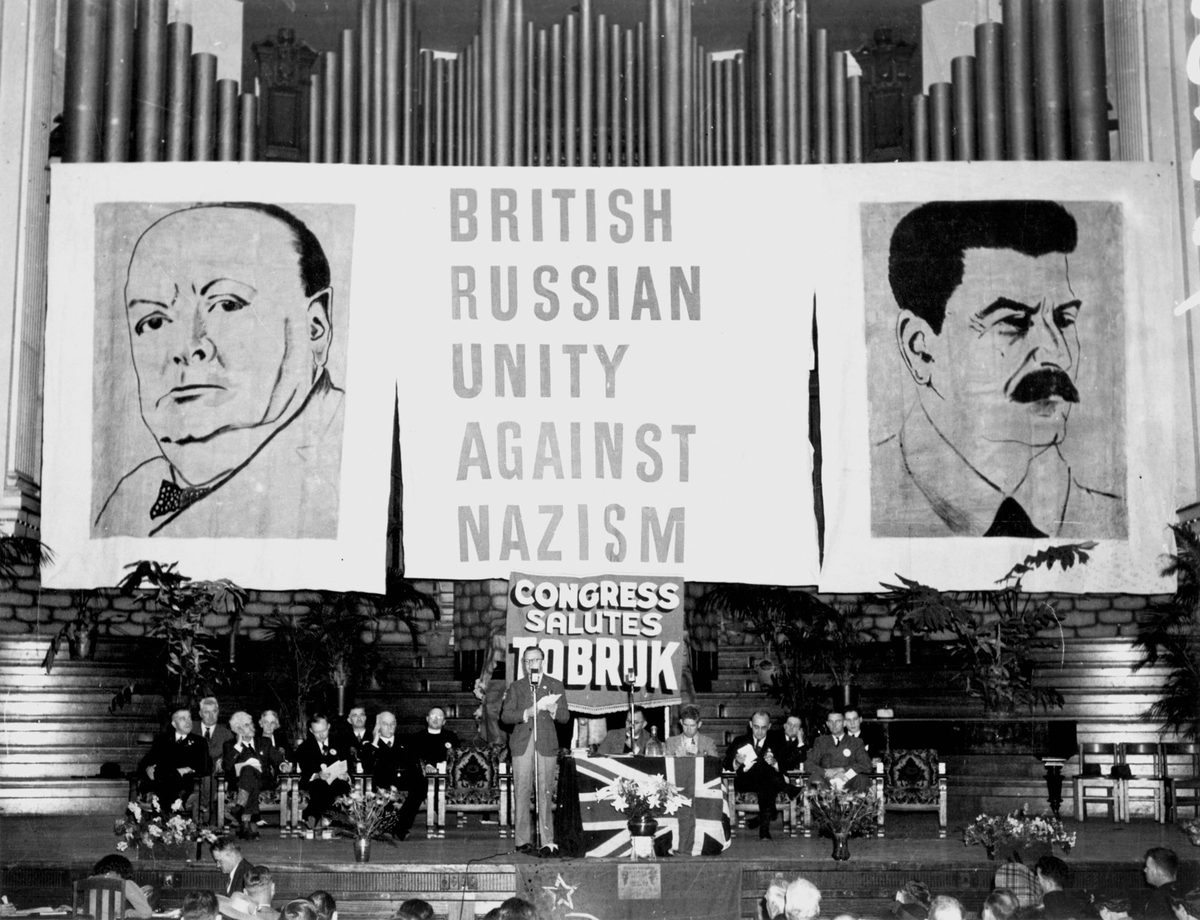 Guests seated on stage in front of a backdrop of giant posters at the Aid to Soviet Congress, Brisbane City Hall, October 1941.