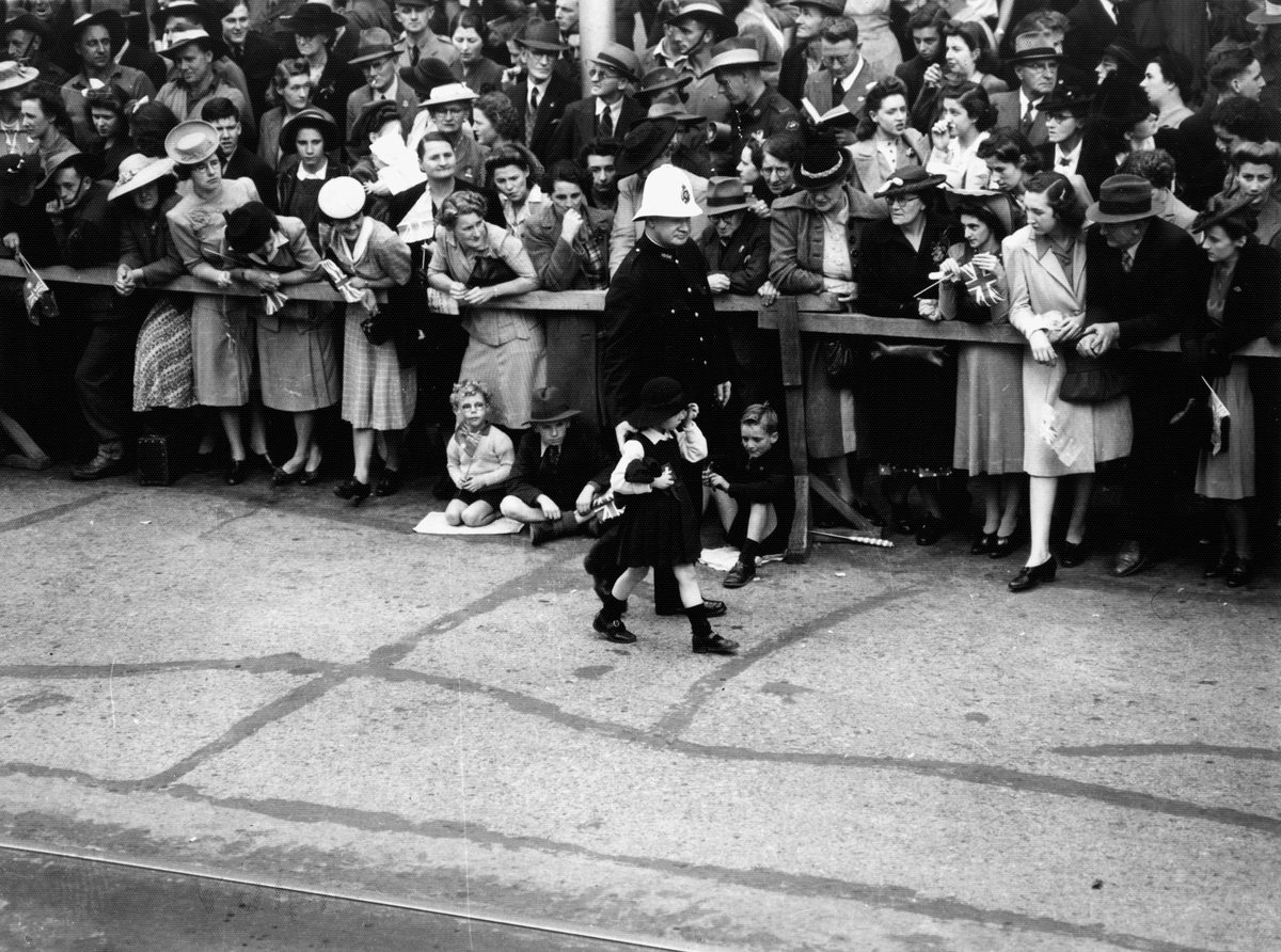 Policeman assists a small girl who is part of the crowd waiting to see the military procession, Brisbane August 1940