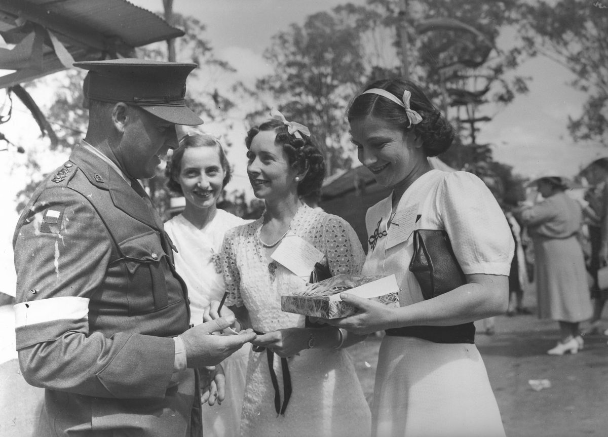 Three girls selling tickets to an officer at Red Cross Fete Government House, 1940
