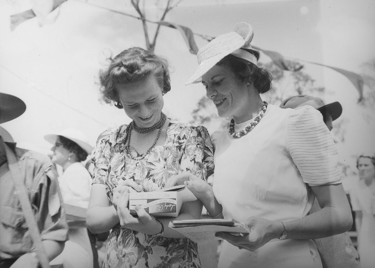 Two women smiling as they add ticket sales at Red Cross Fete Government House, 1940