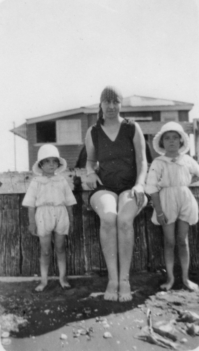Woman and two small girls sitting on the retaining wall at Cribb Island beach, 1928
