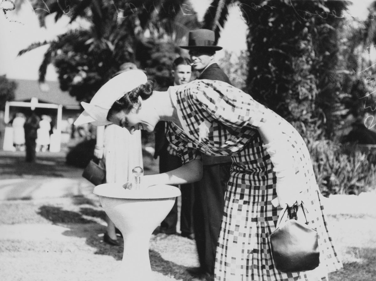 Woman enjoying a drink from the fountain at the Albion Park racecourse, Brisbane, 1939