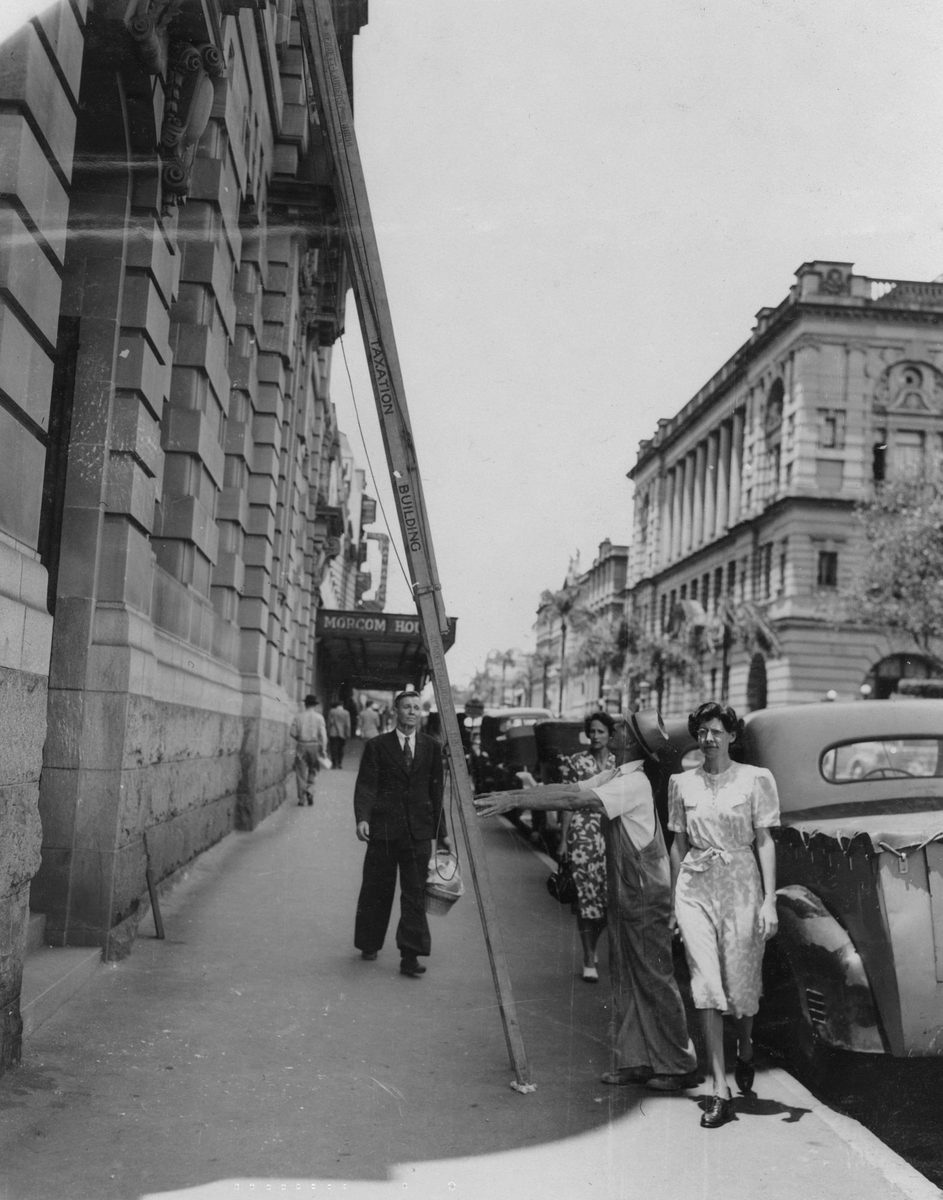 Workman supporting a ladder on George Street, Brisbane, 1949